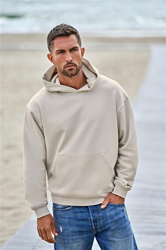 Man wearing a beige Tee Jays Label Free hoodie walking on the beach.