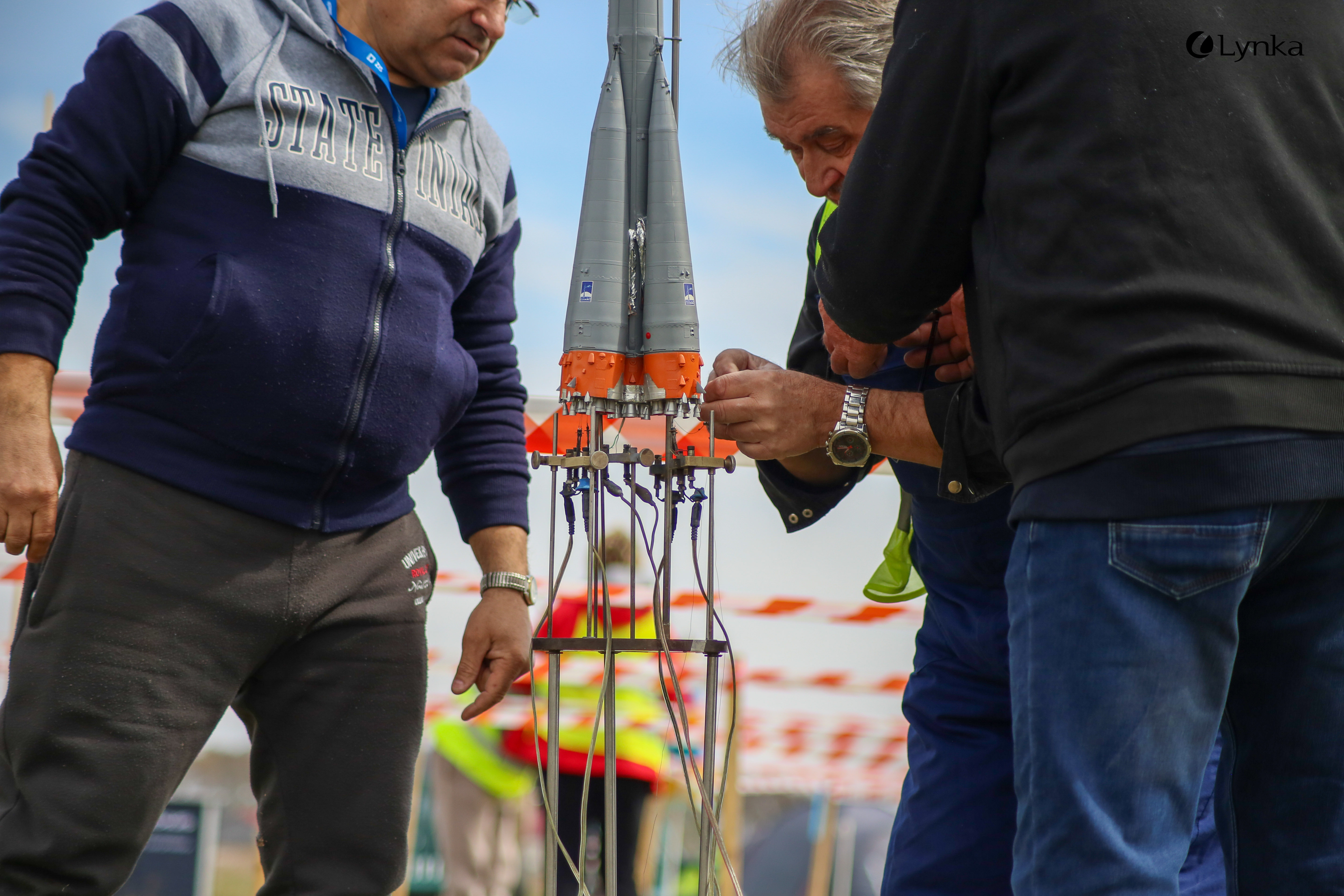 Close-up of hands preparing a detailed multi-stage model rocket on a launch pad during a modeling competitio