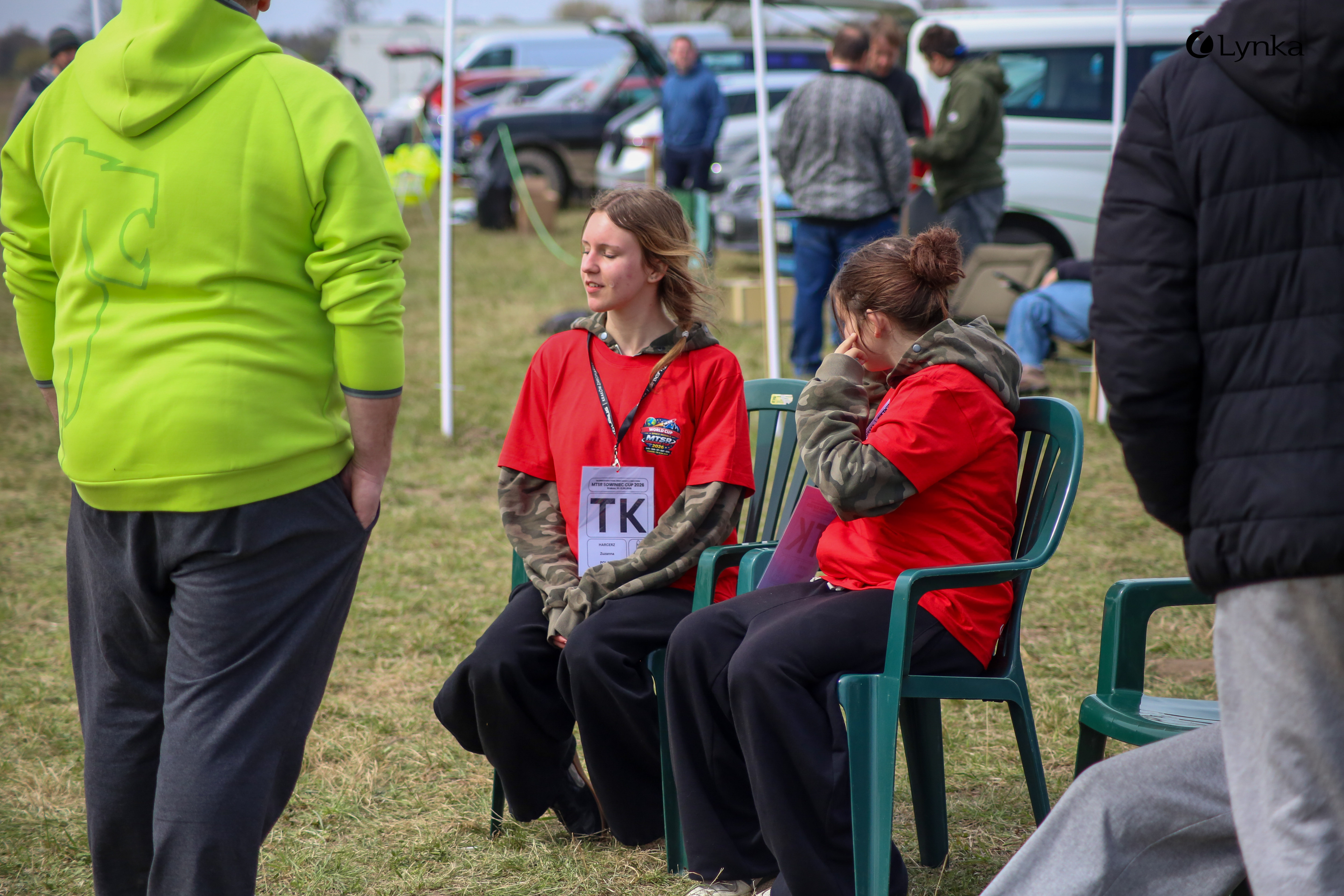 Two participants in red MTSR T-shirts sitting on chairs during a break at the outdoor space modeling competition.