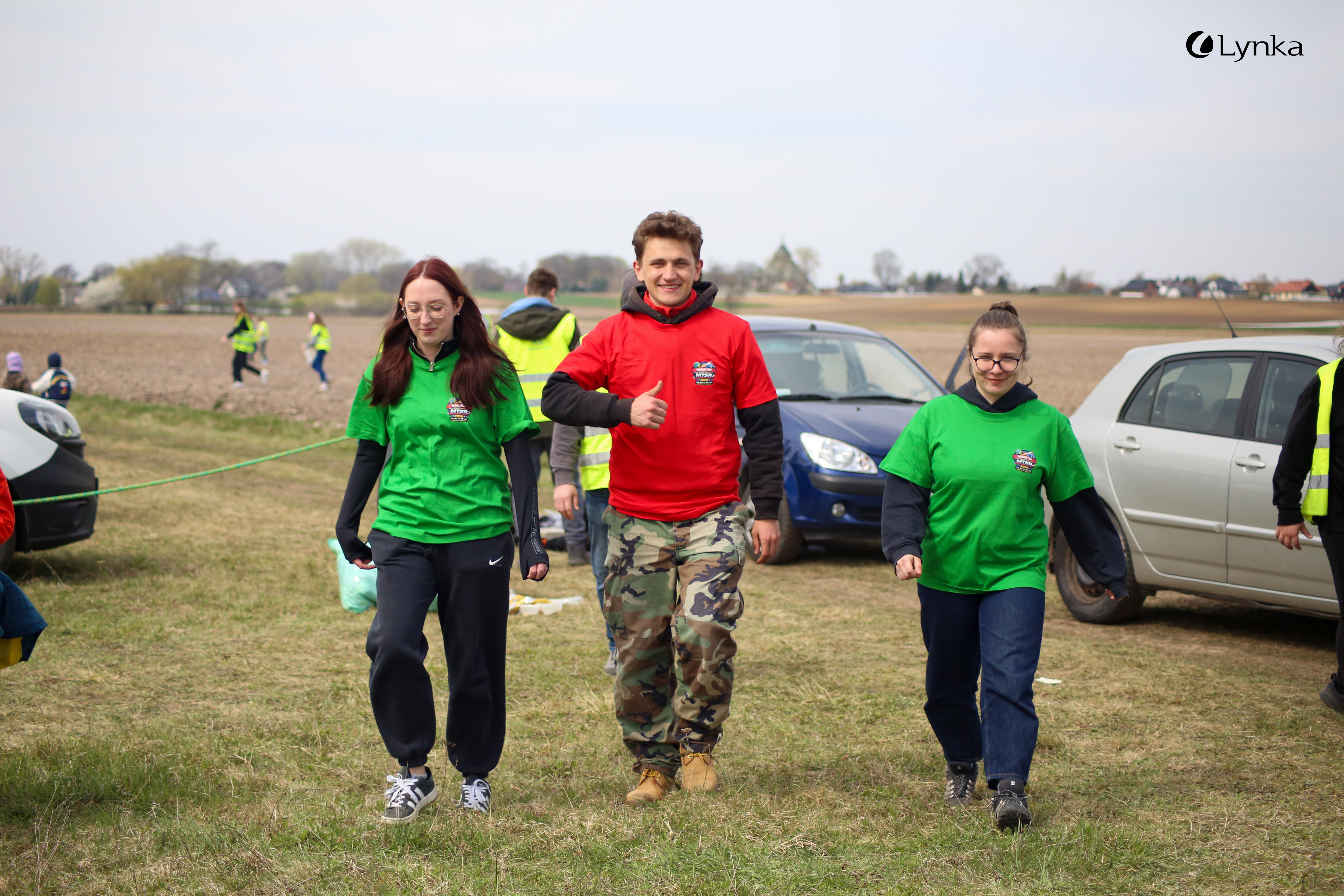 Three smiling participants in colorful event T-shirts walking across a field during the MTSR 2026 competition.