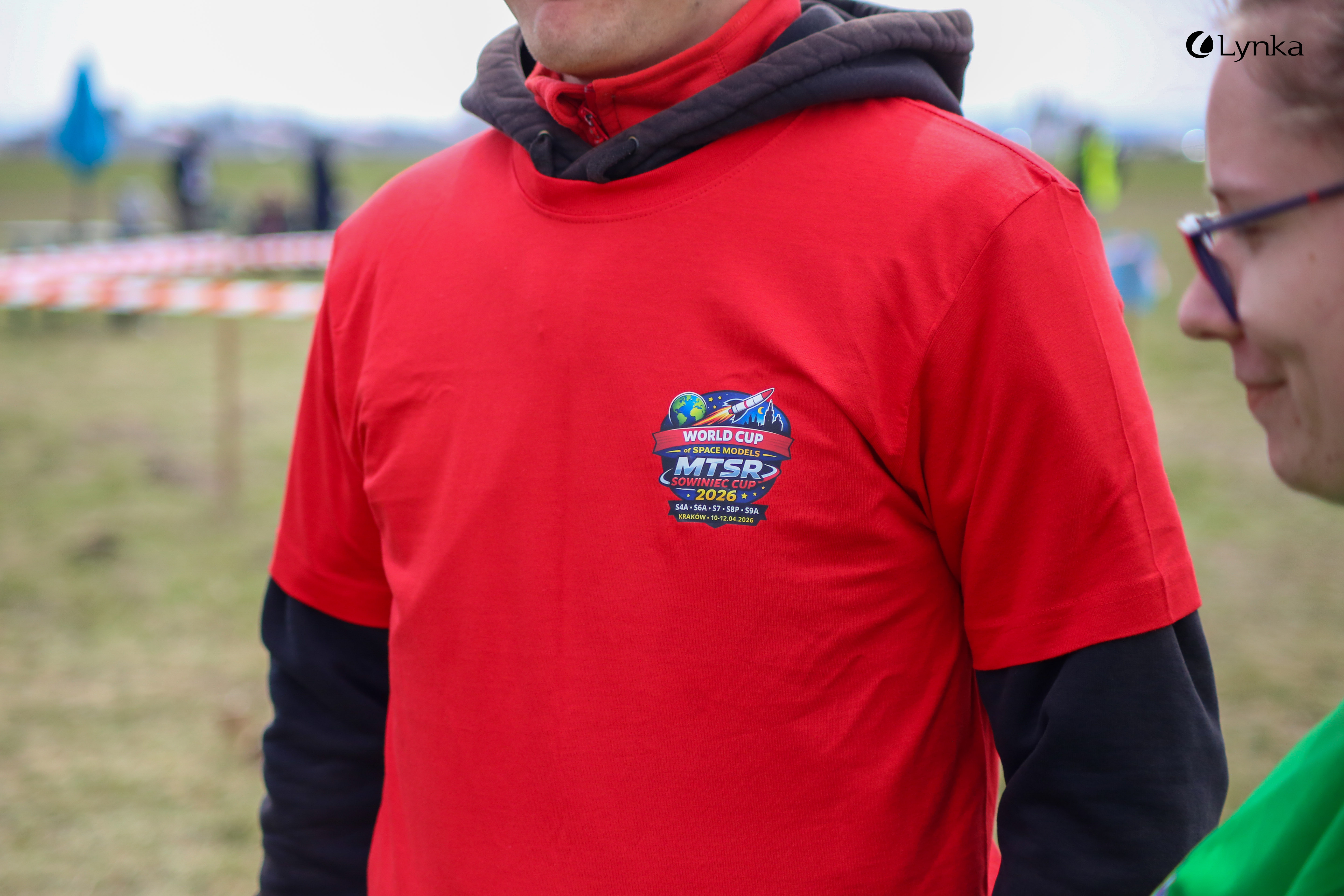 Zbliżenie na logo "World Cup of Space Models MTSR Sowiniec Cup 2026" nadrukowane na czerwonej koszulce eventowej.