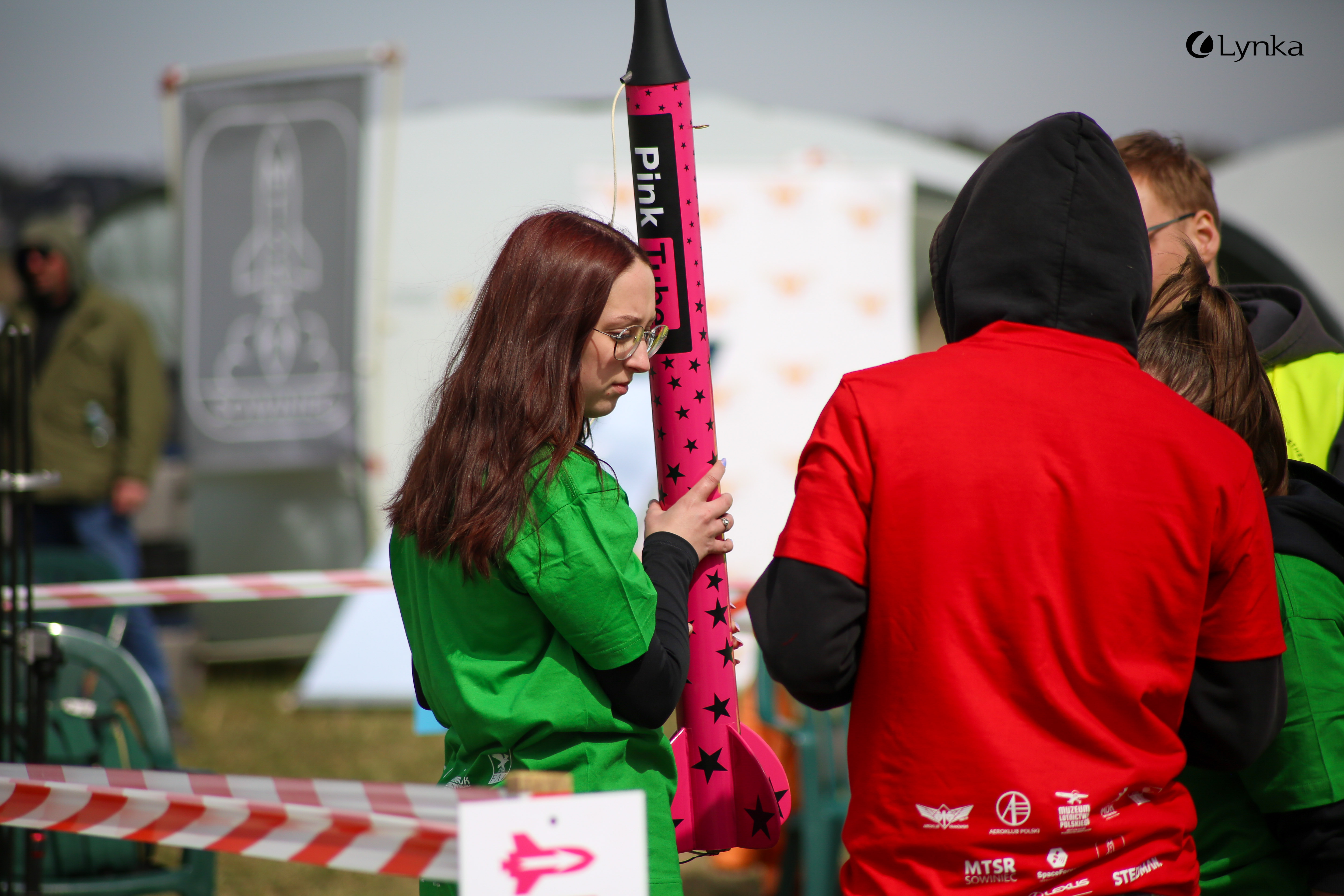 Woman in a green T-shirt holding a pink model rocket decorated with stars during the MTSR 2026 space modeling competition.
