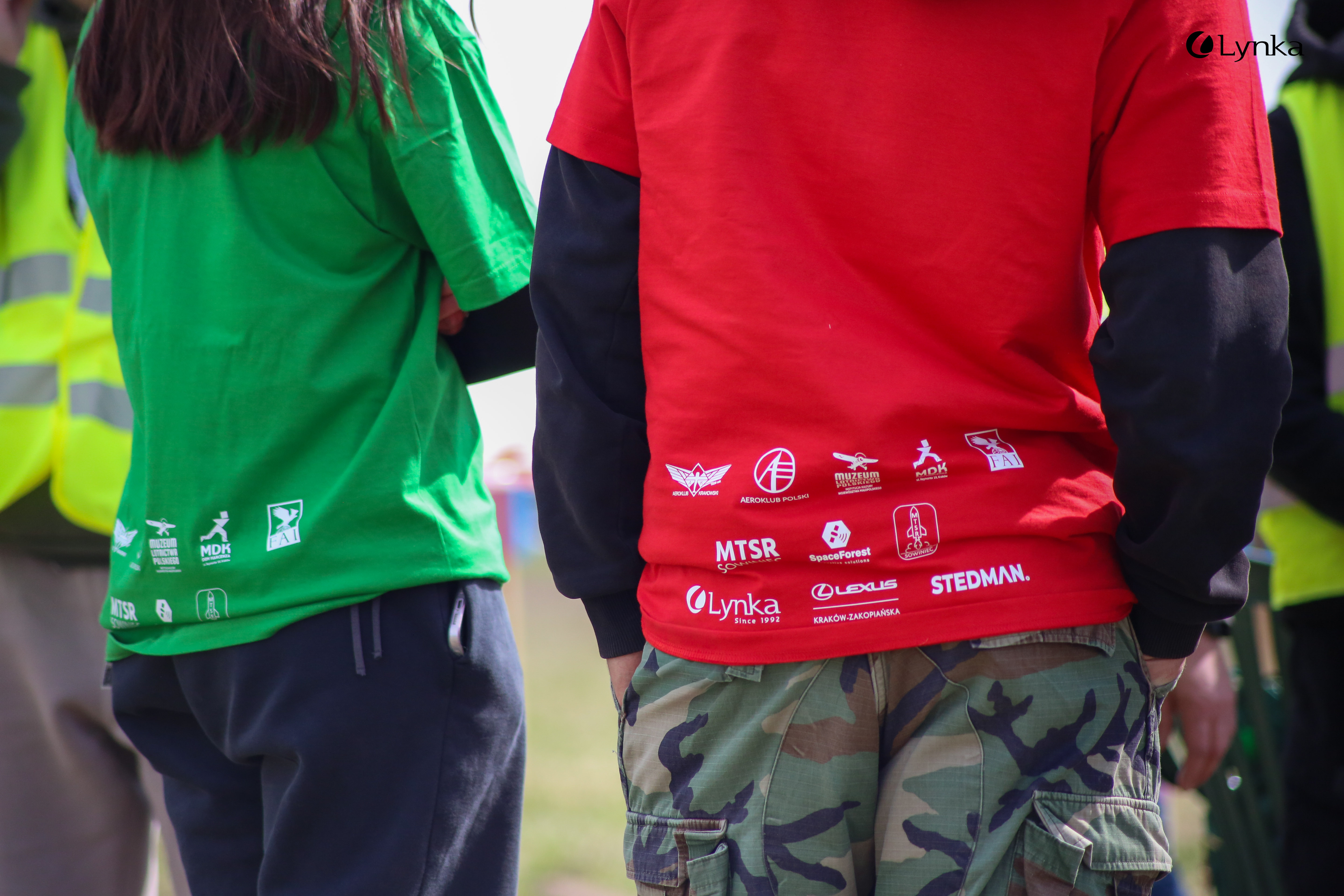 Back of a red and green event T-shirts featuring logos of sponsors and partners like Lynka, Stedman, Lexus, and MTSR.