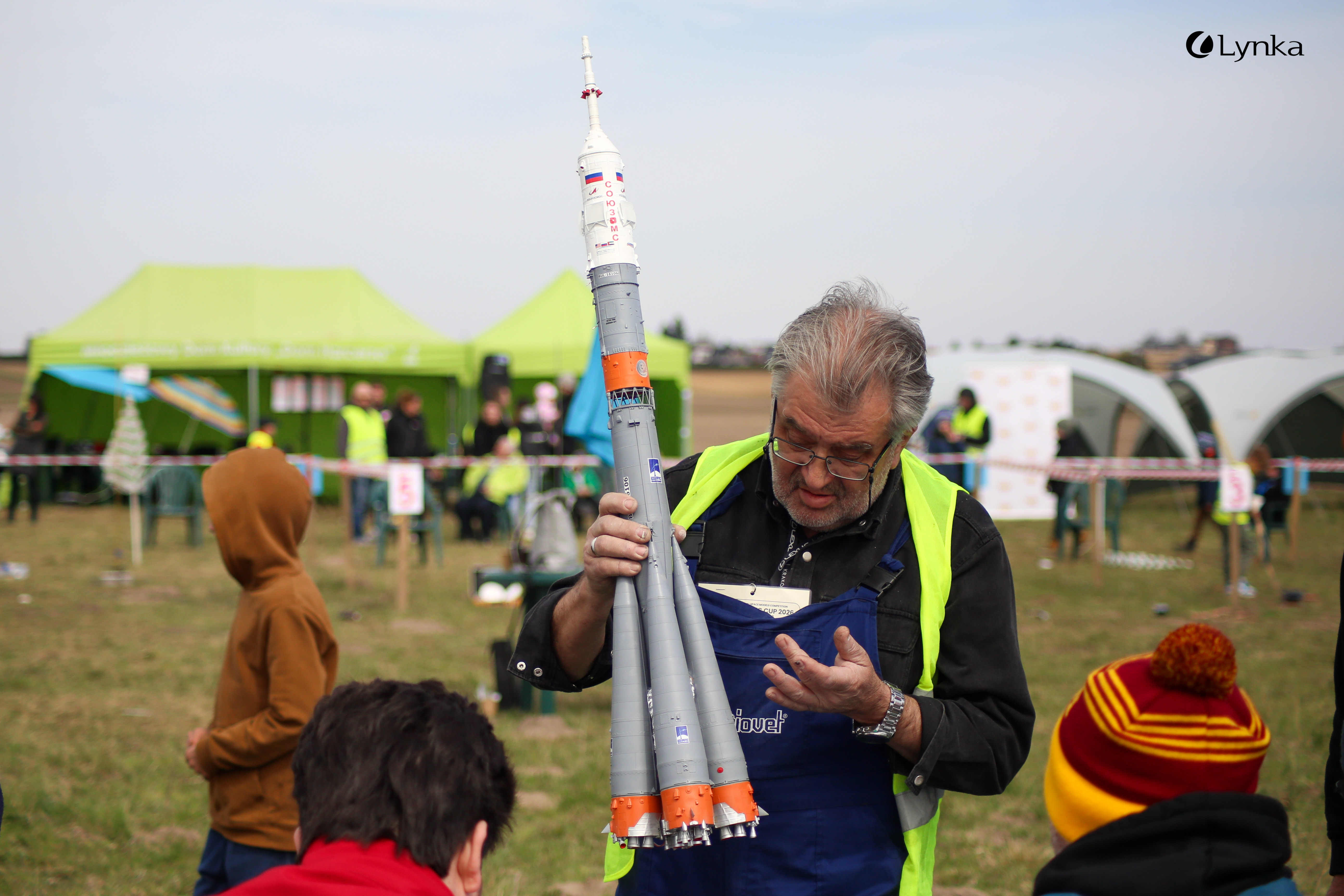 Man in a yellow safety vest holding a detailed gray model of a multi-stage rocket at the MTSR 2026 competition.